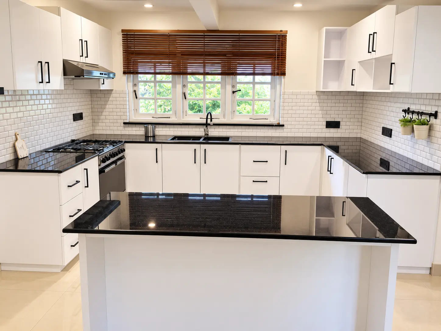 White U-shaped kitchen with black stone island and timber blinds